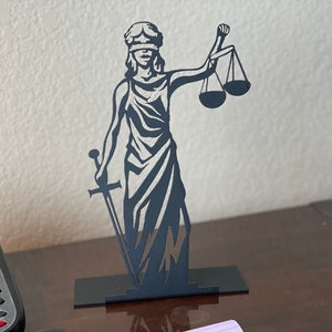 May include: Black metal sculpture of the figure of Justice, holding a sword and scales. The figure is blindfolded and wearing a robe.