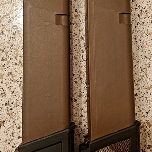 May include: Two brown magazine extensions for a firearm. The extension on the left has a black base, while the extension on the right has a brown camouflage base.