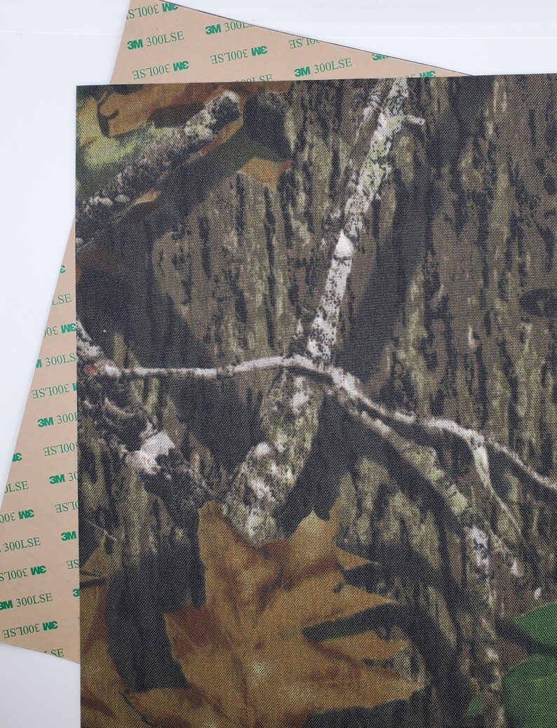 May include: Camouflage fabric with a brown, green, and tan pattern. The fabric has a textured surface and is designed to blend in with the surrounding environment.