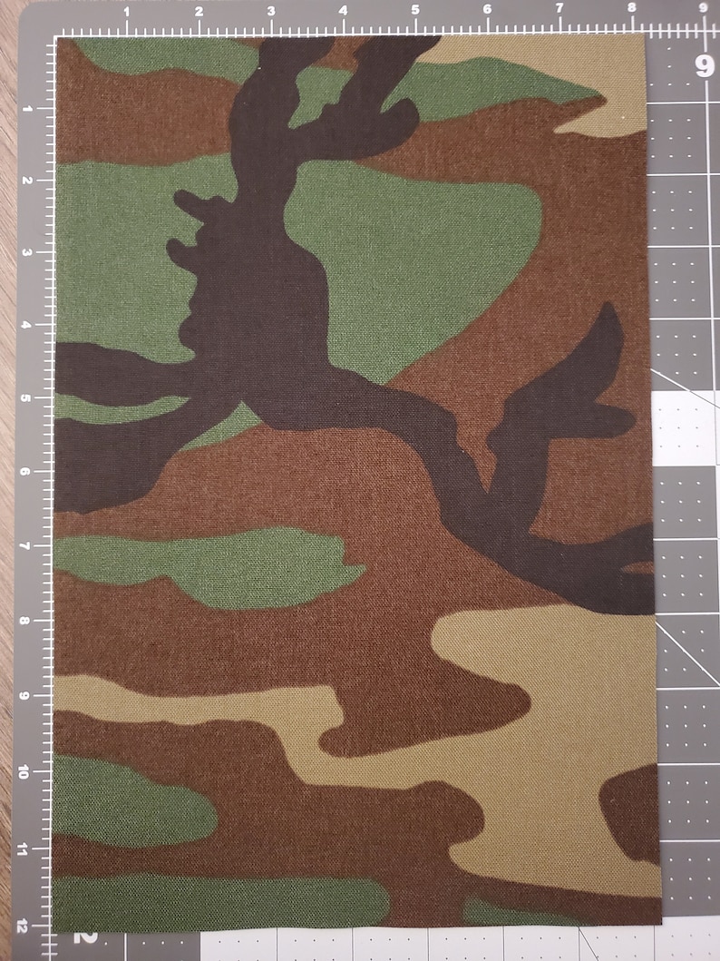 May include: A close-up of a camouflage fabric with brown, green, and tan colors. The fabric has a woven texture and is suitable for crafting projects.