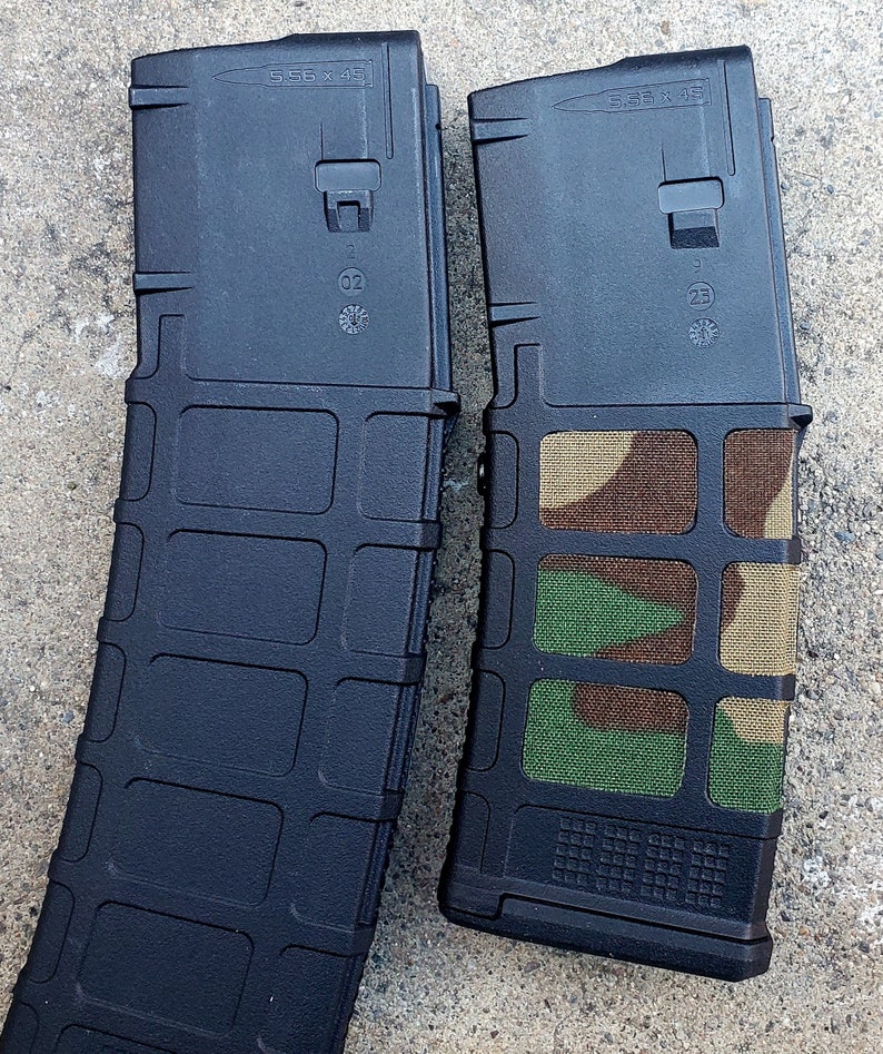 May include: Two black 5.56 x 45 magazines. One magazine has a camouflage pattern covering the front and sides. The text "5.56 x 45" is printed on the top of both magazines.