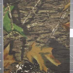 May include: Camouflage fabric with a brown, green, and tan pattern. The fabric has a woven texture and a subtle sheen.