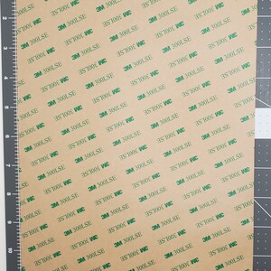 May include: A sheet of brown adhesive tape with a repeating pattern of green 3M 300LSE labels. The tape is marked with measurements in inches.
