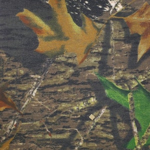 May include: Camouflage fabric with a brown, green, and white pattern. The fabric features a textured weave and a realistic depiction of leaves and branches.