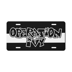 May include: Black and white license plate with the words "OPERATION IVY" in a graffiti-style font. The text is outlined in white and set against a black background with a white stripe across the center.