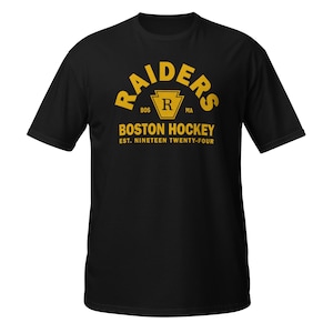 Könnte beinhalten: Ein schwarzes Kurzarm-T-Shirt mit gelbem Grafikdruck. Das Design zeigt den Text RAIDERS in einem Bogen, ein zentrales Wappen mit dem Buchstaben R, den Text BOSTON HOCKEY und den Text EST. NINETEEN TWENTY-FOUR unter dem Wappen.
