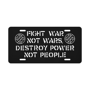 May include: Black license plate with white text that reads "FIGHT WAR NOT WARS, DESTROY POWER NOT PEOPLE." The plate features two circular graphics. The plate has four mounting holes.