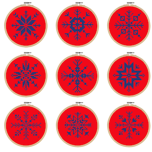 May include: Nine cross-stitch embroidery hoops featuring snowflake designs. Each design is a different pattern in blue against a red background. The hoops are round with wooden frames, perfect for holiday decor or winter crafts.