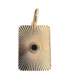 May include: Gold-colored rectangular pendant with a sunburst design. The pendant has a circular center and radiating lines. A small gold clasp is attached at the top. The pendant is likely made of metal and is suitable for jewelry.