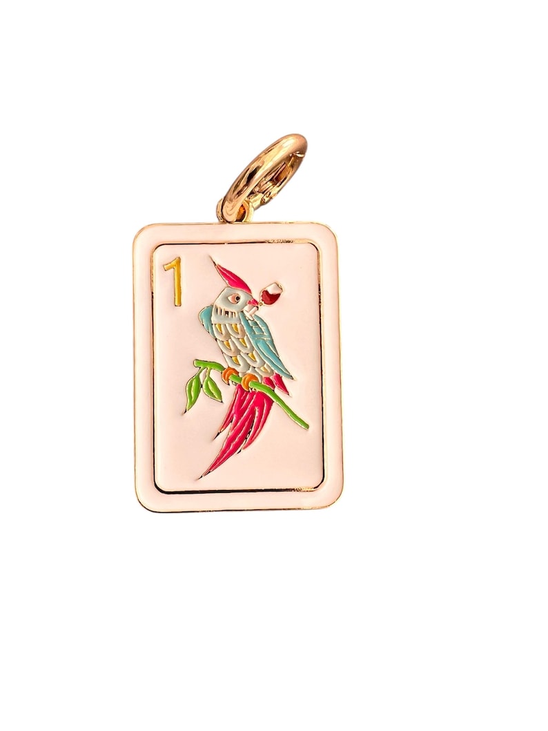 May include: A rectangular pendant with a gold-colored bail. The pendant features a parrot illustration with red, blue, and green details, perched on a branch. The number "1" is displayed in gold. The background is a light pink color.