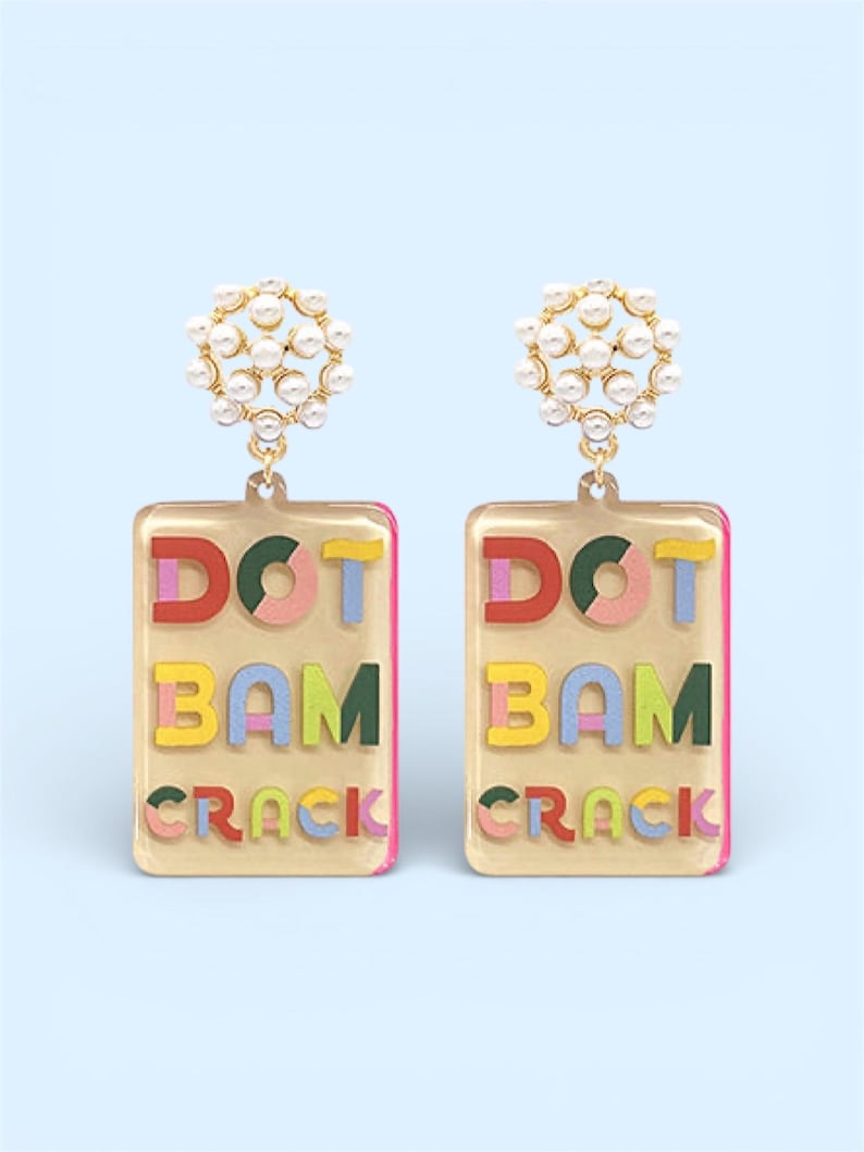 K&ouml;nnte beinhalten: Ein Paar goldfarbene Ohrringe mit rechteckigem Design. Jeder Ohrring zeigt die Worte "DOT BAM CRACK" in bunten Buchstaben. Die Oberseite jedes Ohrrings hat eine Ansammlung kleiner, wei&szlig;er Perlen.