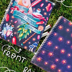 May include: A spiral-bound coloring book with a dark blue cover featuring the text "Spells & Potions Coloring Book." The cover design includes illustrations of crystals, potions, mushrooms, and a crescent moon. The back cover has a pattern of red stars.