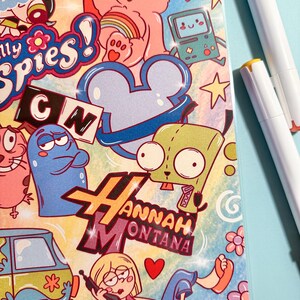 Puede incluir: Un colorido libro para colorear con una variedad de personajes de dibujos animados y el texto "Prints Coloring Book". La portada presenta personajes de varios programas animados, incluyendo un Care Bear rosa, un dise&ntilde;o azul en forma de rat&oacute;n y las palabras "Hannah Montana."