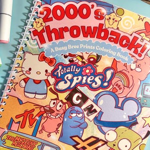 Puede incluir: Un libro para colorear con espiral titulado "2000's Throwback!" con personajes de dibujos animados como Hello Kitty, Coraje el perro cobarde y personajes de Totally Spies! y Hannah Montana. La portada es colorida con un fondo azul claro.