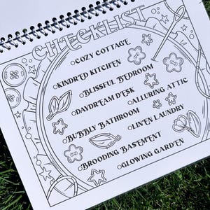 May include: A spiral-bound notebook with a black and white checklist design. The word "CHECKLIST" is at the top, with themed room names like "Cozy Cottage" and "Glowing Garden" listed below. Decorative elements include stars, flowers, and sewing tools.
