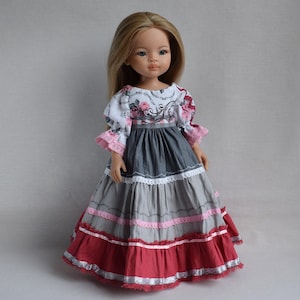 Könnte beinhalten: Eine Puppe mit langem blondem Haar trägt ein Kleid mit weißem Oberteil mit rosa-grauem Blumenmuster, Puffärmeln und einem mehrstufigen Rock in Grau- und Dunkelrottönen, verziert mit weißen und rosa Spitzenbesätzen an den Säumen.