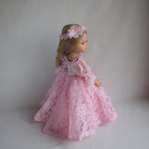 Può includere: Un vestito di pizzo rosa con un corpetto di pizzo bianco e una corona di fiori su una bambola.