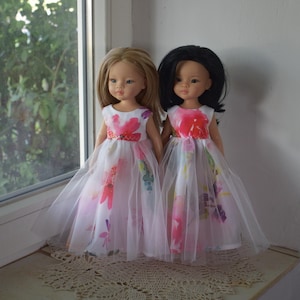 May include: Two dolls in white dresses with floral patterns and tulle skirts. One doll has blonde hair, the other has black hair. The dresses feature pink, red, and purple floral designs.