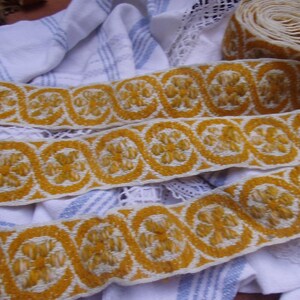 Può includere: Primo piano di nastro decorativo tessuto giallo e bianco con motivo floreale. Il nastro è in rotolo e anche steso. Il nastro è su un panno bianco e blu a righe.