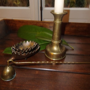 May include: A brass candlestick with a white candle, a brass hedgehog-shaped ashtray, and a brass candle snuffer on a wooden surface.