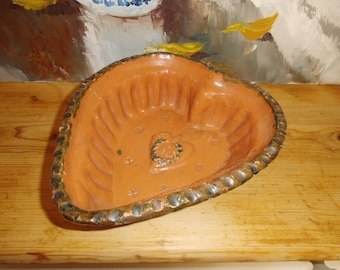 Op de afbeelding: Een hartvormige terracotta vorm met een groene geglazuurde rand en een hartontwerp in het midden. De vorm heeft een geribbeld interieur.