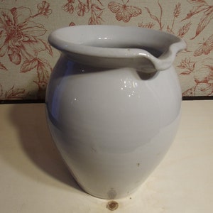 May include: A white ceramic pitcher with a slightly chipped rim. The pitcher has a smooth, rounded body and a slightly flared lip.