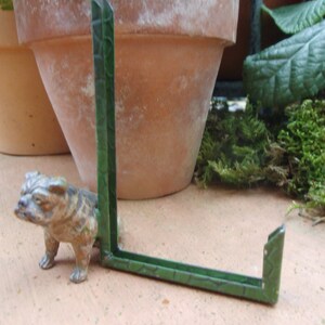 Könnte beinhalten: Ein grüner Bilderrahmen aus Metall mit einer Bulldoggenfigur davor. Der Rahmen besteht aus zwei Teilen, die zusammenklappbar sind.