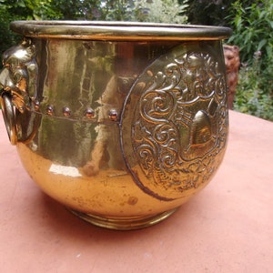 Peut inclure: Un grand pot de fleurs en laiton antique avec une tête de lion d'un côté et un motif orné de l'autre. Le pot a une forme arrondie et une surface lisse et polie.