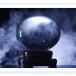 May include: A clear crystal ball sits on a dark wooden stand, surrounded by swirling white smoke against a black background. The sphere reflects light, creating a mystical and ethereal atmosphere. The image evokes themes of fortune-telling and divination.