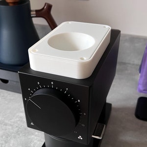 May include: A black electric coffee grinder with a white removable hopper and a dial with numbers 3 through 11. The grinder is on a grey countertop.