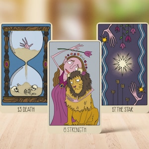 May include: Three tarot cards featuring illustrated designs. The left card shows an hourglass with skulls and a hand, labeled 13 DEATH. The center card depicts a figure embracing a lion, labeled 8 STRENGTH. The right card shows a star, labeled 17 THE STAR.