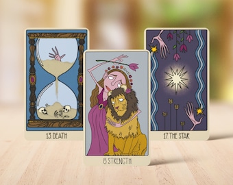 Op de afbeelding: Drie tarotkaarten met geïllustreerde ontwerpen. De linkerkaart toont een zandloper met schedels en een hand, gelabeld 13 DEATH. De middelste kaart toont een figuur die een leeuw omhelst, gelabeld 8 STRENGTH. De rechterkaart toont een ster, gelabeld 17 THE STAR.