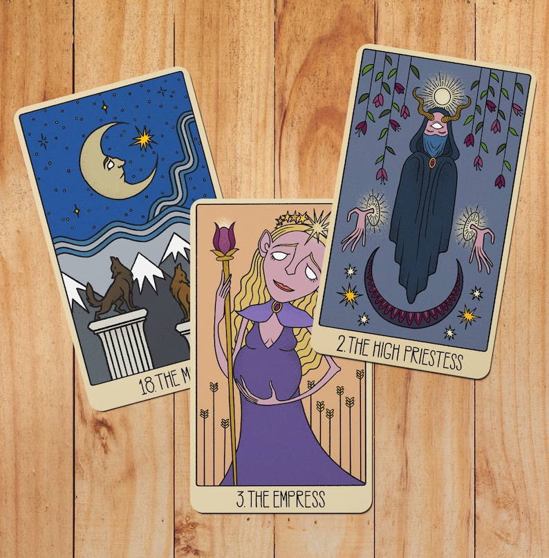 May include: Three tarot cards featuring illustrated designs. The left card shows a moon, mountains, and wolves labeled 18. THE MOON. The center card depicts a figure with long hair holding a staff labeled 3. THE EMPRESS. The right card shows a hooded figure labeled 2. THE HIGH PRIESTESS.