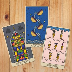 May include: Three tarot cards featuring Five of Pentacles with a stained glass window design, 14 Temperance showing water pouring between cups against a starry blue sky, and Seven of Cups displaying various objects in golden chalices on pink clouds.