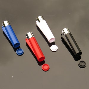 Peut inclure: Quatre briquets cylindriques bleus, rouges, blancs et noirs, chacun avec un dessus en métal argenté et un clip de couleur assortie. Les briquets sont présentés avec leurs bouchons amovibles, également de couleurs assorties.