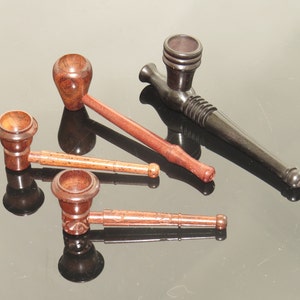 May include: A collection of wooden pipes in shades of brown and black. The pipes have rounded bowls and slender stems, some with carved patterns. They are displayed on a reflective surface, with their reflections visible.
