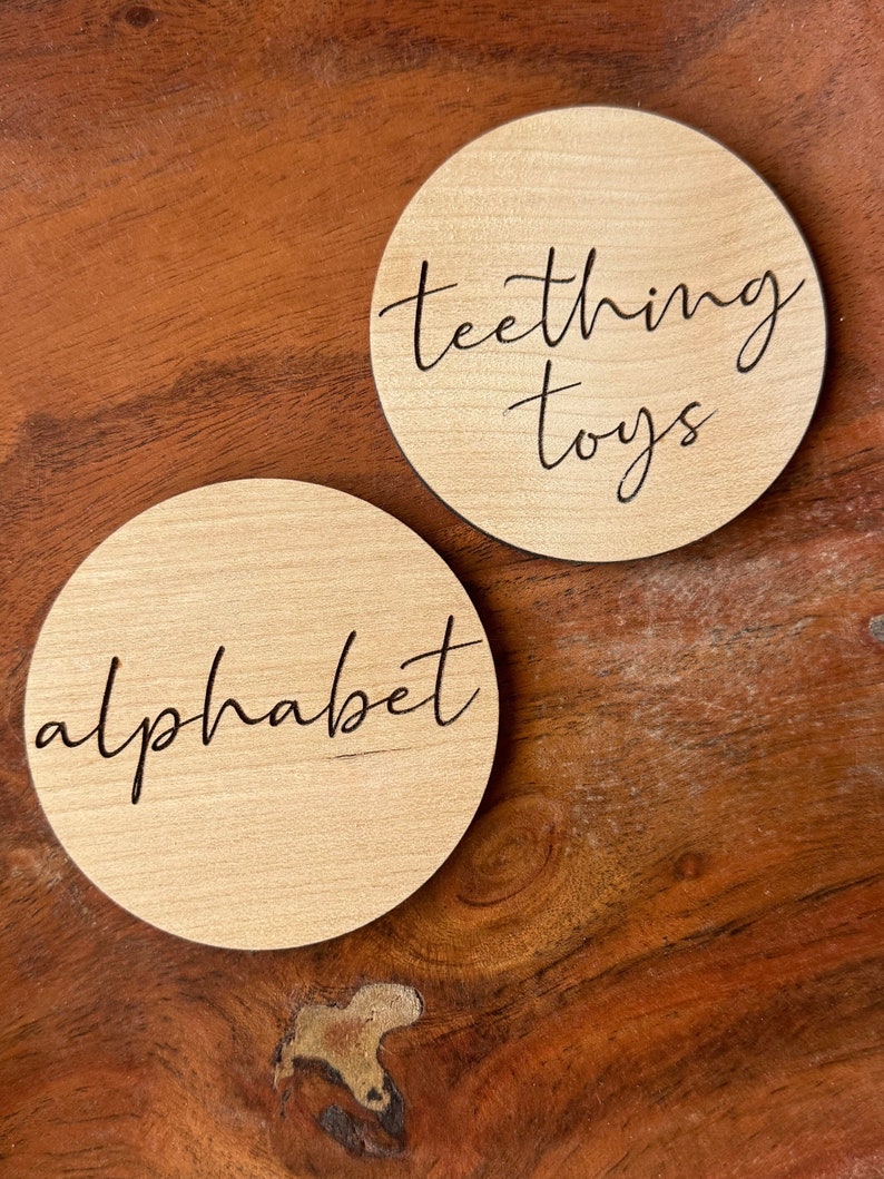 May include: Two round wooden signs with black lettering. One sign says "teething toys" and the other says "alphabet".