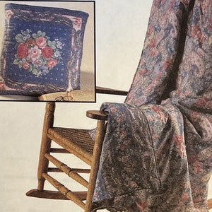 May include: A rocking chair with a floral patterned throw blanket draped over it. The blanket has a paisley design with pink, blue, and white colors. A matching floral patterned pillow is on the floor next to the chair.