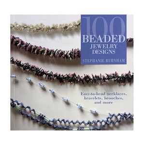 May include: Book cover featuring 100 Beaded Jewelry Designs by Stephanie Burnham. The cover shows four beaded necklaces in various colors and styles, including white, pink, black, and blue.