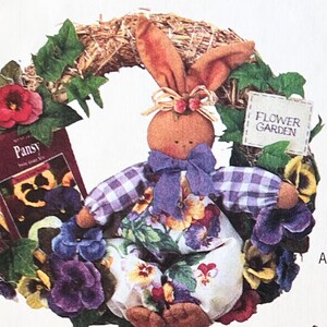 May include: A handmade wreath featuring a purple and white gingham bunny holding a book titled "Pansy" with the text "Flower Garden" on a sign. The wreath is decorated with purple, yellow, and red pansies.