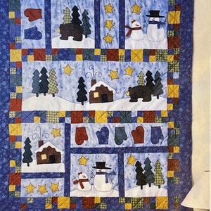 May include: A blue and yellow patchwork quilt with a winter theme. The quilt features bears, snowmen, cabins, and trees.