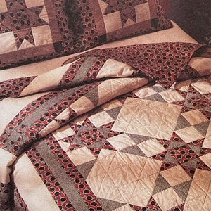 May include: A beige and red quilt with a star pattern. The quilt is folded on a bed with a matching pillow.