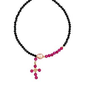 Puede incluir: Un collar de cuentas negras y rosas con un dije de cruz rosa. El collar está hecho con cuentas de ónix negro, cuentas rosas y una sola perla.