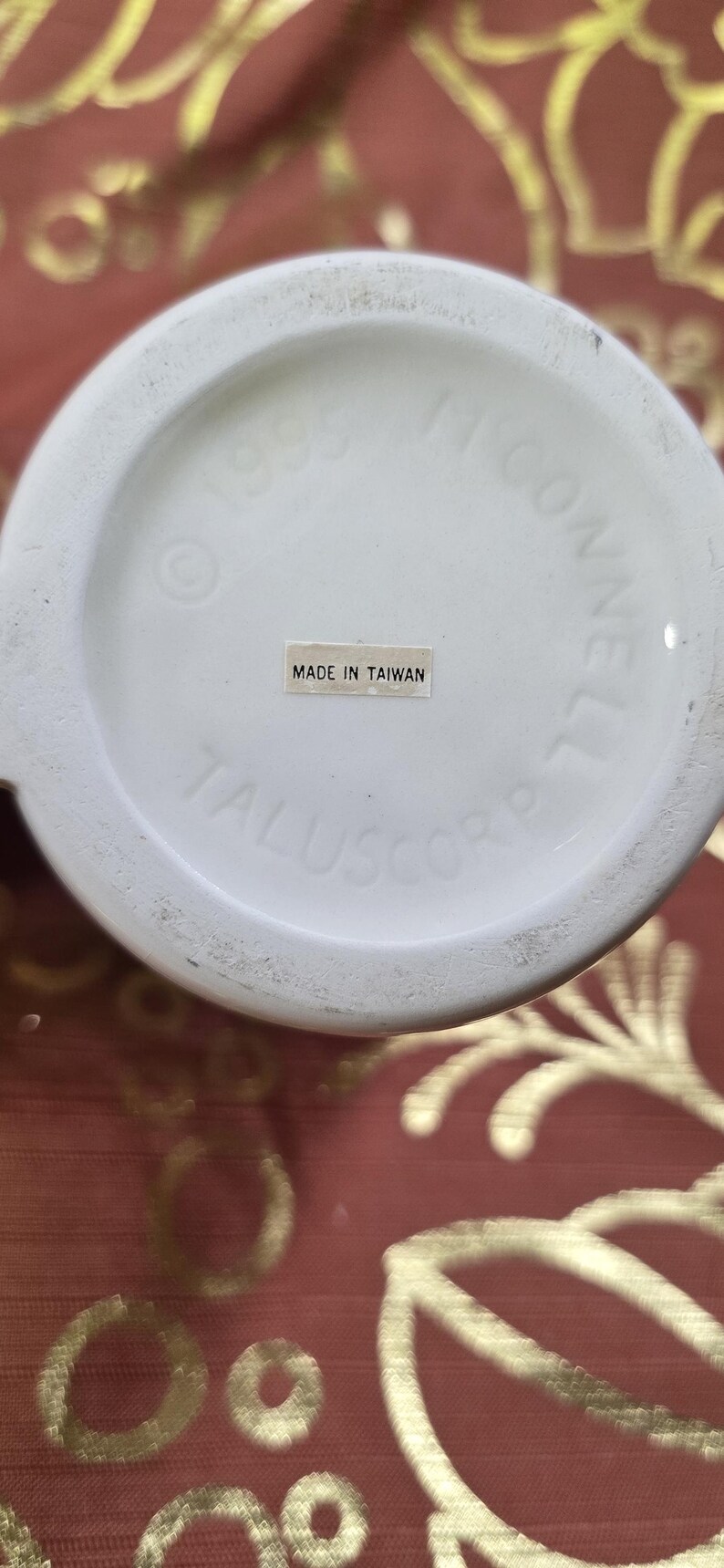 May include: Close-up of the bottom of a white ceramic mug. The text "MADE IN TAIWAN" is visible on a small sticker. The mug's base also includes the text "&copy; 1993 J. CONNELL" and "TALUSCORP".