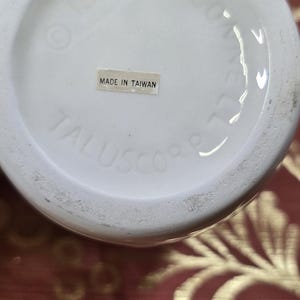 May include: A white ceramic object with the text "MADE IN TAIWAN" on a sticker. The object has the text "TALUSCORP" and "1985" printed on it.