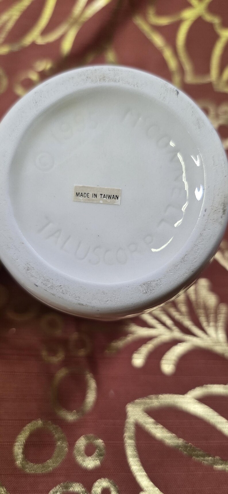 May include: A white ceramic object with the text "MADE IN TAIWAN" on a sticker. The object has the text "TALUSCORP" and "1985" printed on it.
