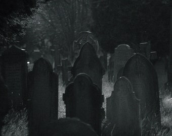 May include: A black and white photograph of a graveyard at night. The headstones are tall and narrow, with some featuring crosses. The image is dark and moody, with a sense of mystery and intrigue.