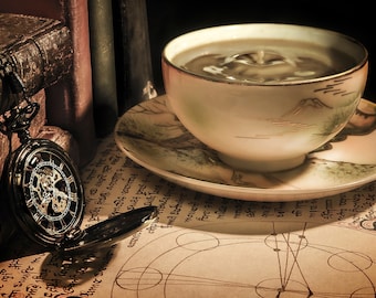 May include: A vintage pocket watch with an intricate clock face sits on an old book with a cup of tea and a saucer with a floral design.