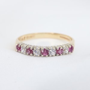 May include: A gold band ring with alternating ruby and diamond stones.