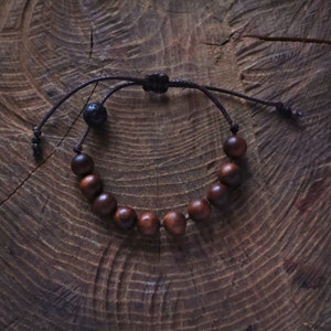 May include: A brown wooden bead bracelet with a black lava rock bead and a brown cord.